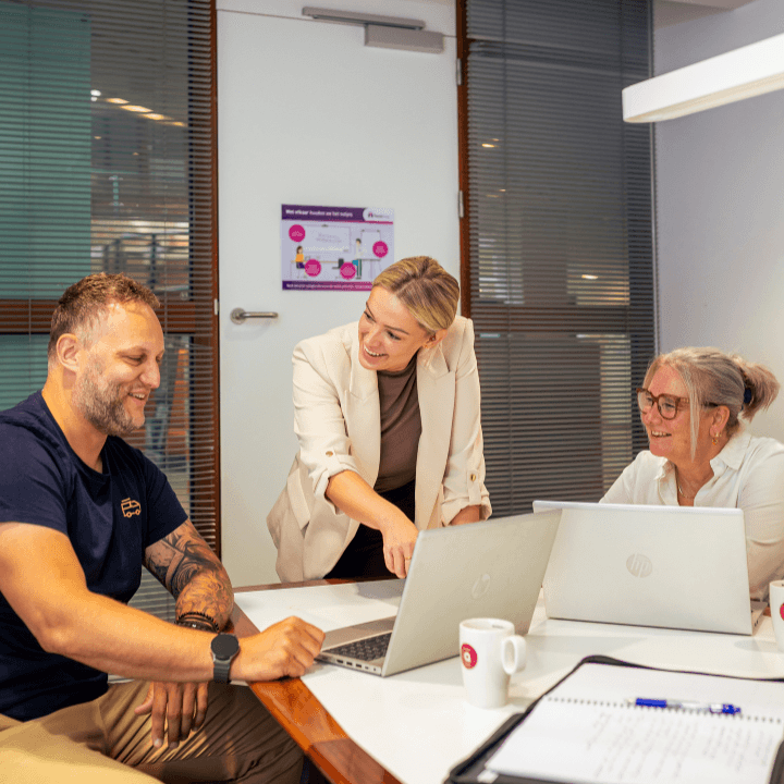 Twee vrouwelijke en een mannelijke medewerkers van MeanderGroep kijken en wijzen naar een laptop in een kantoor.