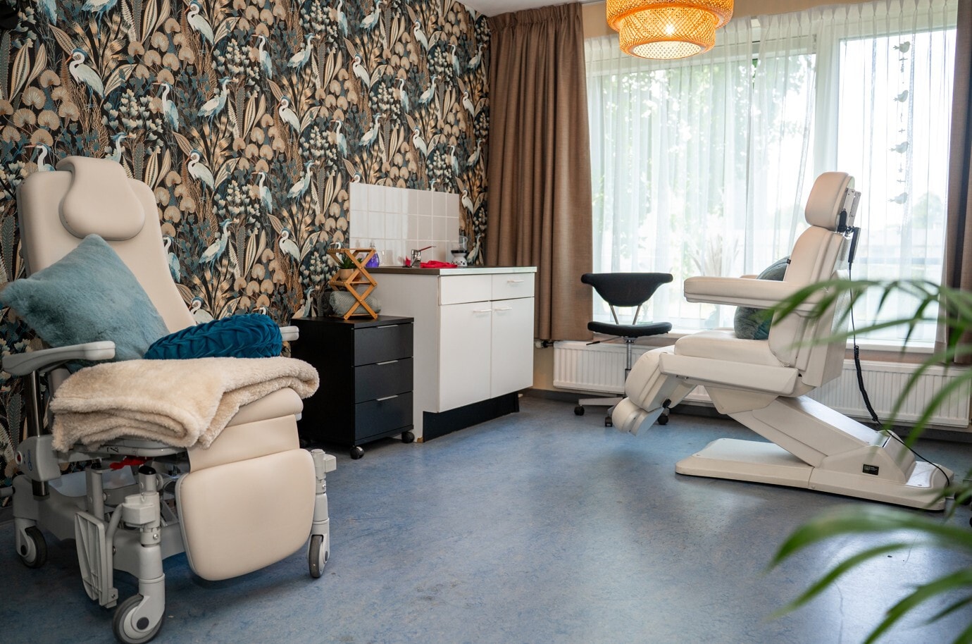Een verzorgde behandelkamer met twee comfortabele witte behandelstoelen en een opvallende wand met vogelpatroon-behang, ingericht voor medische of uiterlijke verzorging.