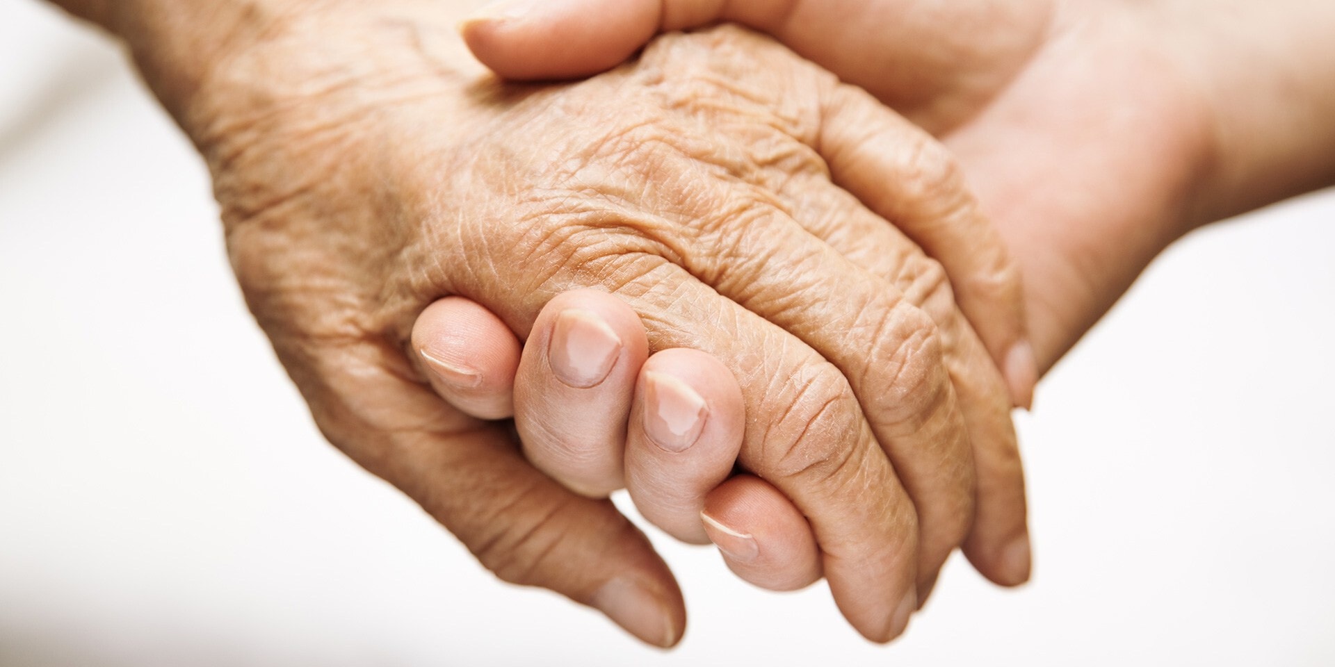 Twee handen houden elkaar vast. De ene hand is van een jonger persoon en de andere hand van een ouder persoon.