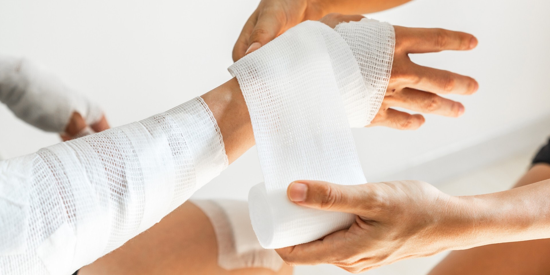 Een hand wikkelt wit gaasverband om de pols en hand van een ander persoon.
