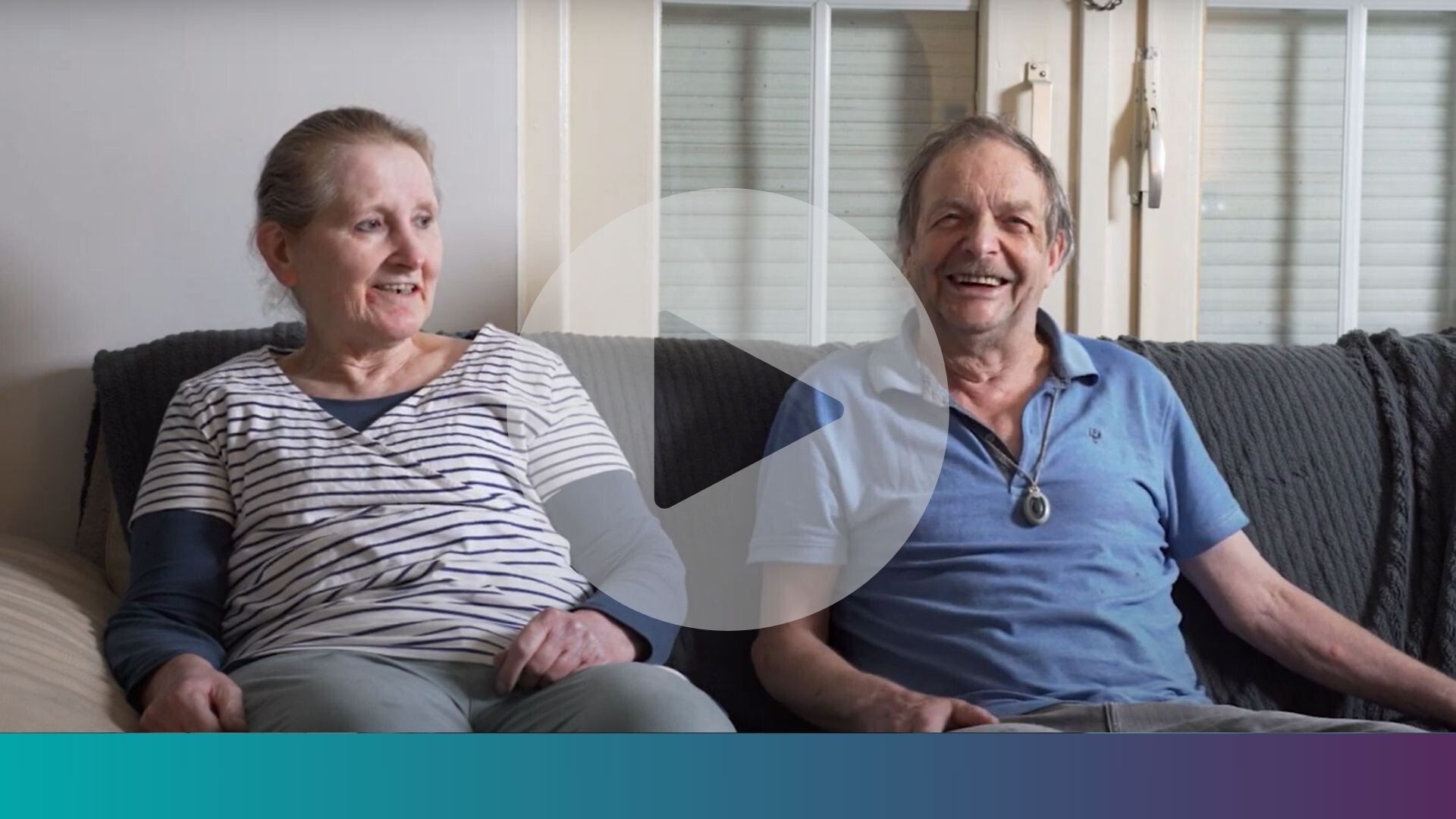 Een lachende oudere man en vrouw zitten op een bank. Over de afbeelding heen staat een grote afspeelknop.