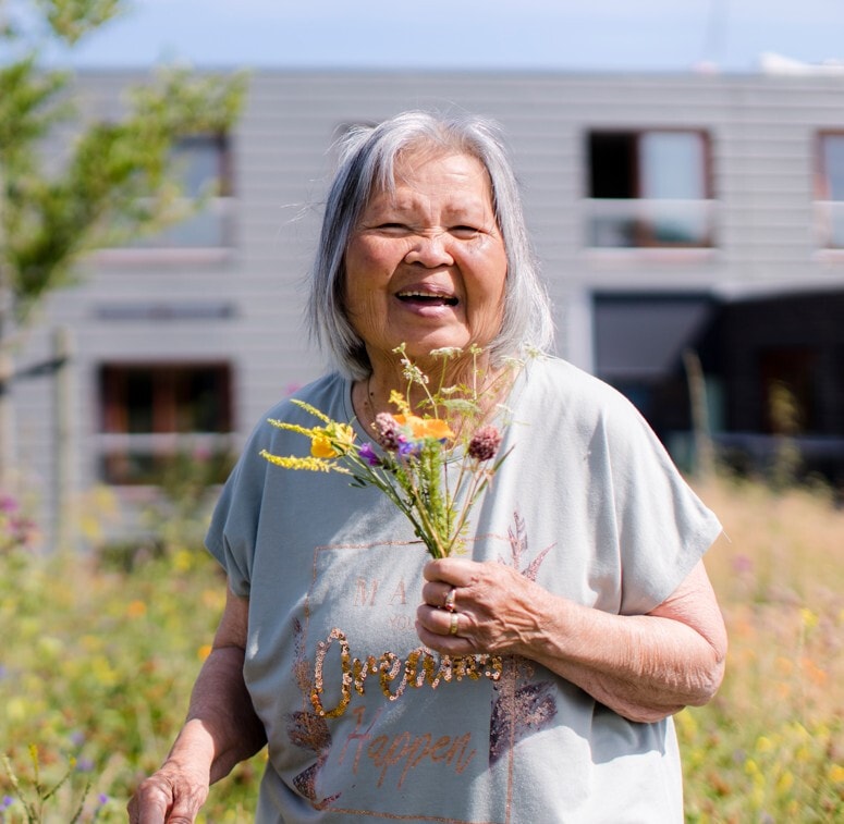 Lachende vrouw met grijze haren die een bosje geplukte bloemen vast heeft.