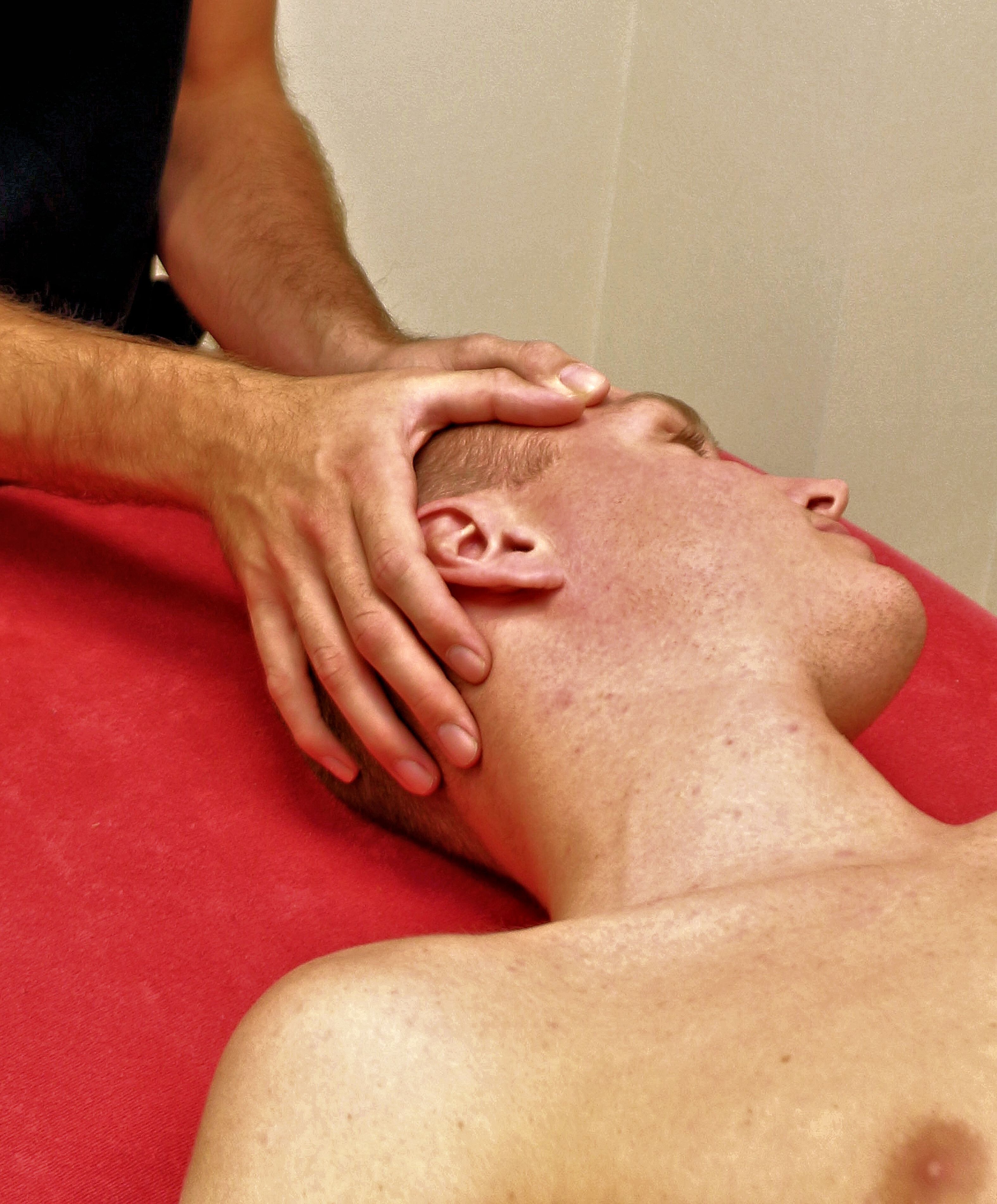 Een close-up van een man die een osteopatische behandeling krijgt terwijl hij op een rode massagetafel ligt.