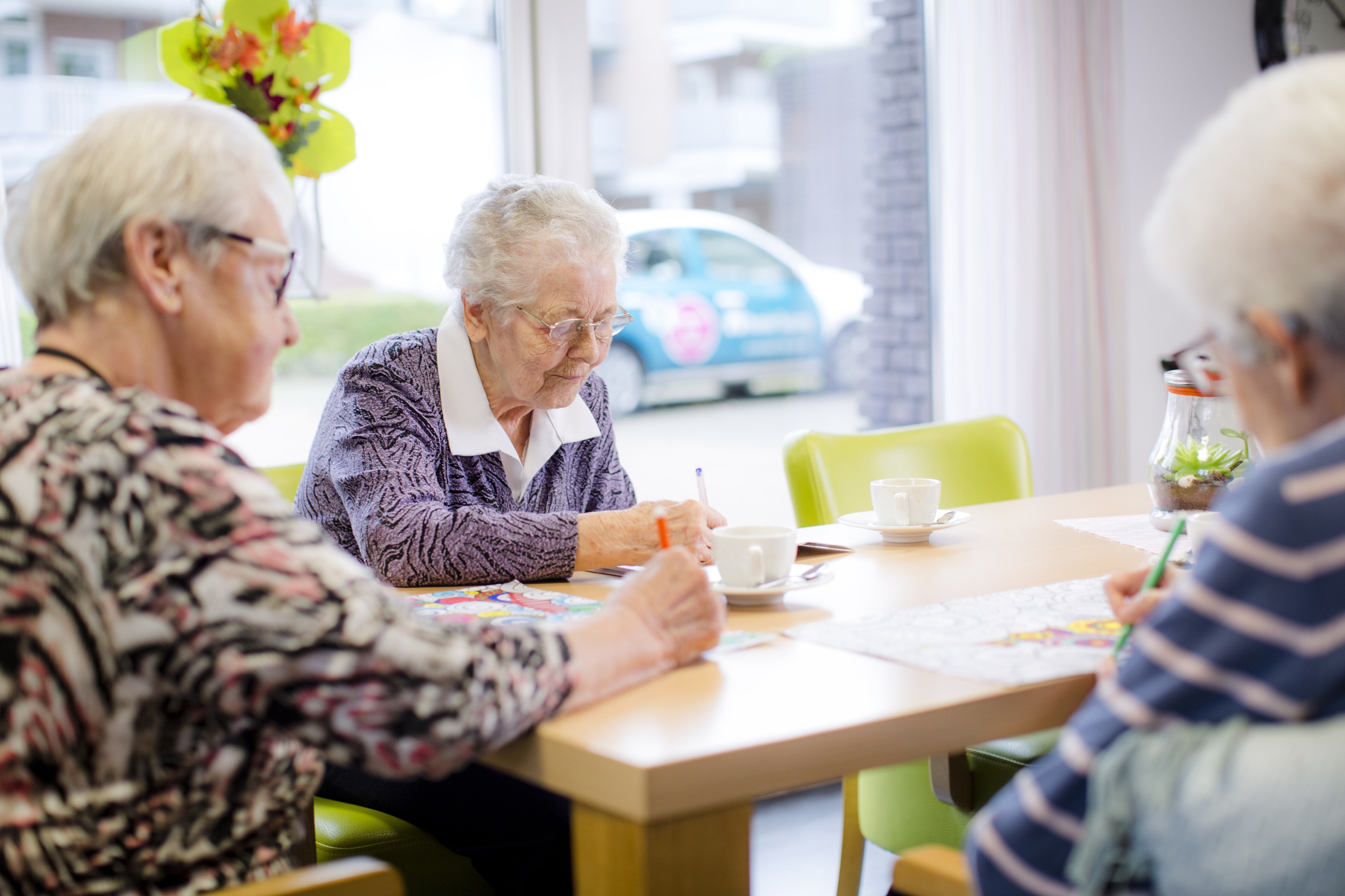 Drie oudere vrouwen zittend aan een tafel kleuren op een kleurplaat.